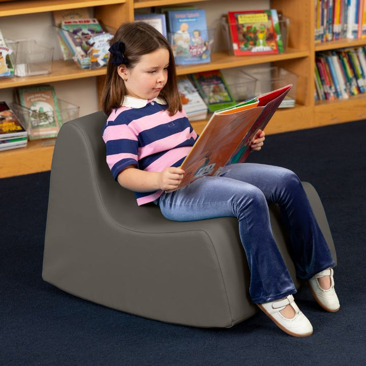 A child reading in the charcoal Jaxx Midtown Rocker, a sensory rocking chair for kids in a school library