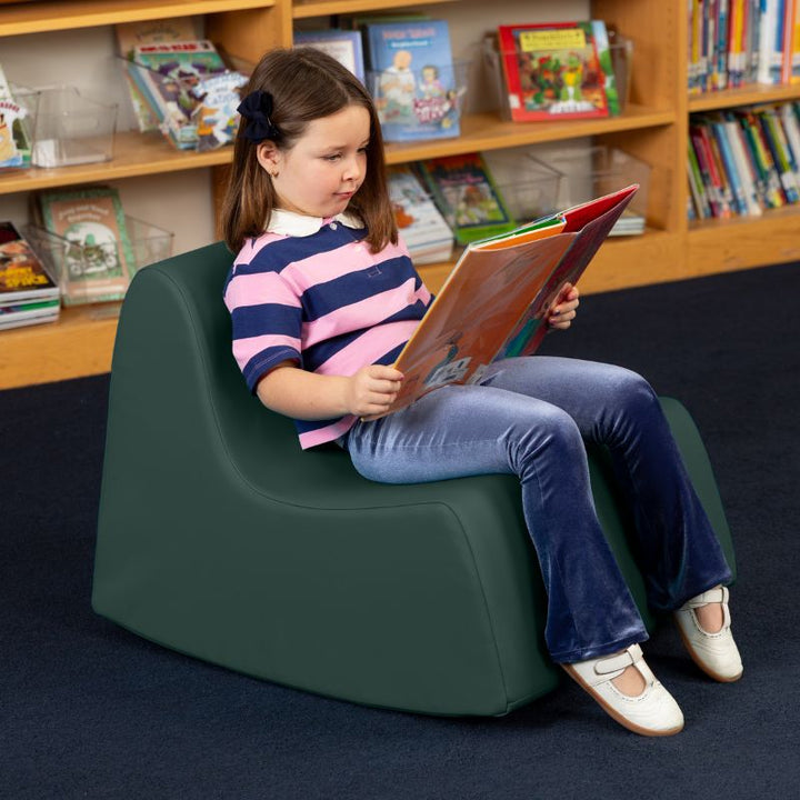 A child reading in the sequoia green Jaxx Midtown Rocker, a sensory rocking chair for kids in a school library