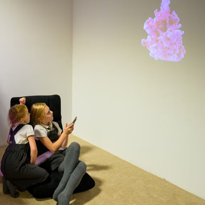 Two children watching a pink cloud themed sensory video from the TFH ChromaTheme system on a calming room wall