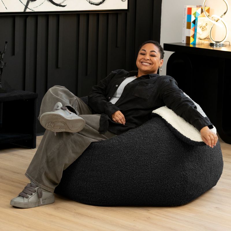 an adult sits comfortably in the black Raven-Symoné HopSeat sherpa bean bag chair at home