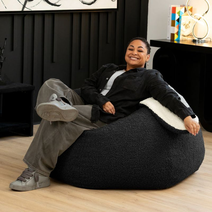 an adult sits comfortably in the black Raven-Symoné HopSeat sherpa bean bag chair at home