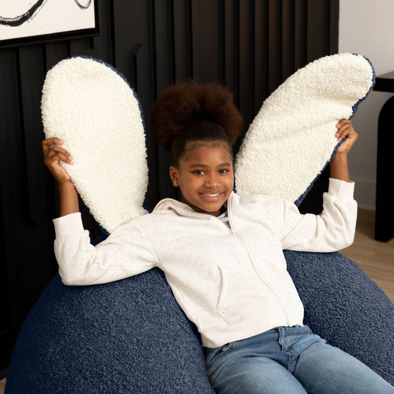 a child sits in the blue Raven-Symoné HopSeat sherpa bean bag chair while holding up its soft, tactile bunny ears