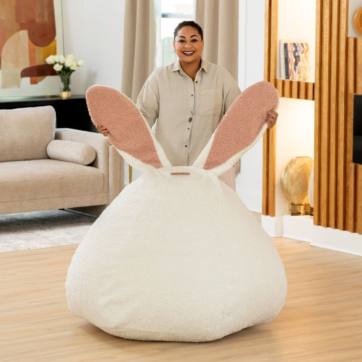 an adult holds up the bunny ears on the Cloud Raven-Symoné HopSeat sherpa bean bag chair in a bright living room