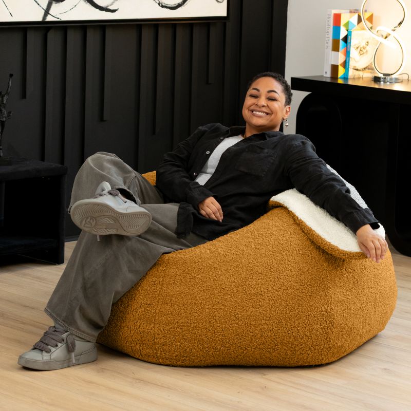 an adult sits comfortably in the gold Raven-Symoné HopSeat sherpa bean bag chair at home