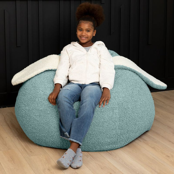 a child relaxes in the green Raven-Symoné HopSeat sherpa bean bag chair, sinking into its deep-pressure comfort