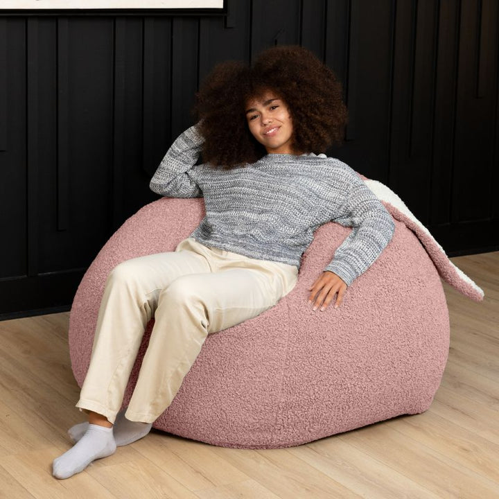 an adult reclines in the pink Raven-Symoné HopSeat sherpa bean bag chair, sinking into its deep-pressure comfort