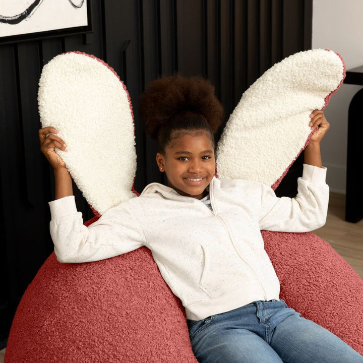 a child sits in the Rosewood Red Raven-Symoné HopSeat sherpa bean bag chair while holding up its soft, tactile bunny ears