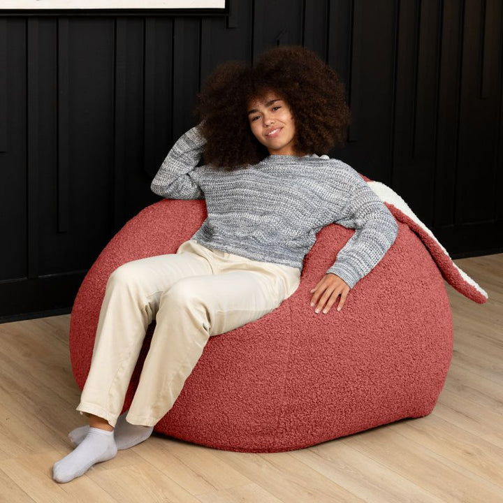 an adult reclines in the Rosewood Red Raven-Symoné HopSeat sherpa bean bag chair, sinking into its deep-pressure comfort