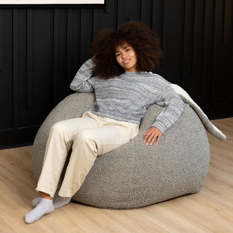 an adult reclines in the Smoke Raven-Symoné HopSeat sherpa bean bag chair, sinking into its deep-pressure comfort