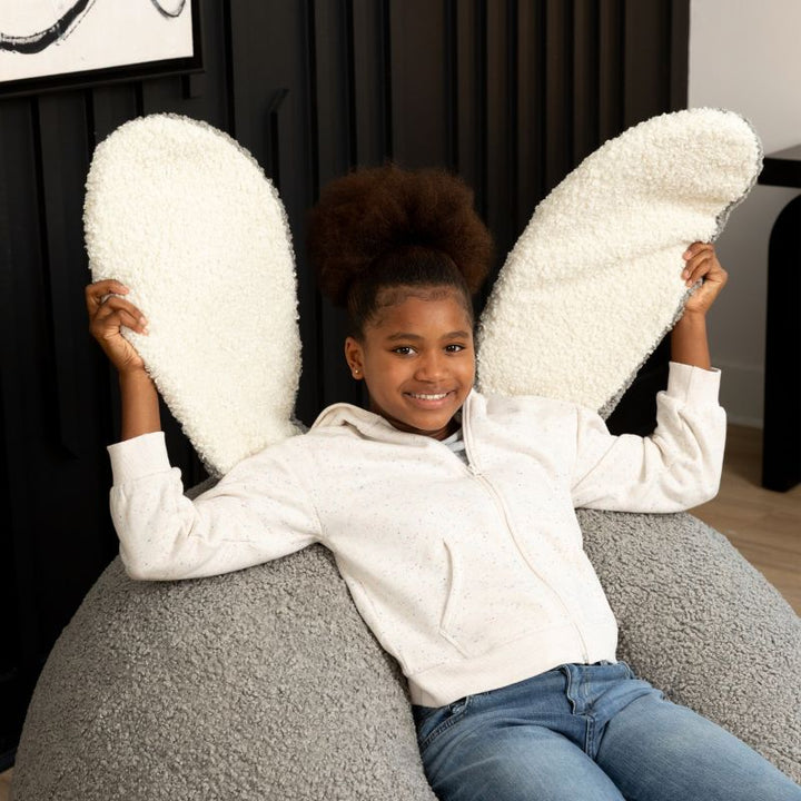 a child sits in the Smoke Raven-Symoné HopSeat sherpa bean bag chair while holding up its soft, tactile bunny ears