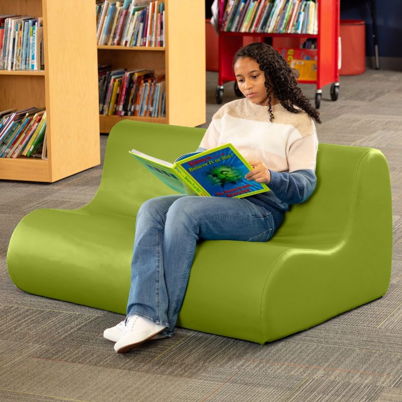A student reading on a green Jaxx Midtown soft seating couch in a school library setting