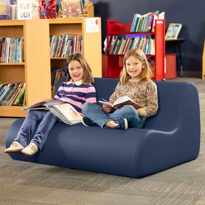 Two children reading on a navy blue Jaxx Midtown soft seating couch in a school library calm corner