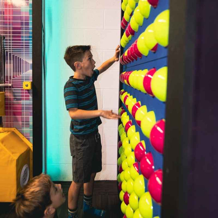 A boy reaching to rotate a sphere on the LiteZilla Spinfinity Wall interactive spinning wall panel in a colourful indoor installation