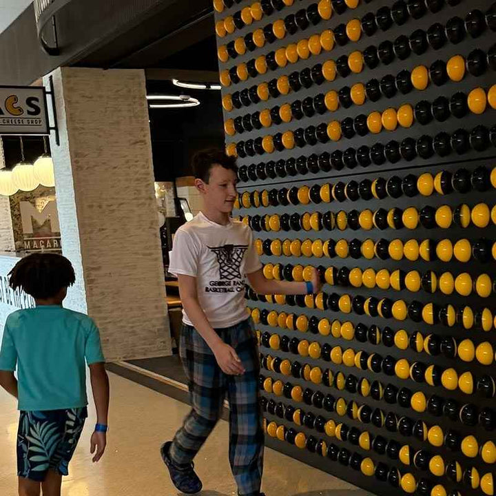 LiteZilla Spinfinity Wall interactive spinning wall panel installed in a mall with children walking past the black and yellow sphere pattern