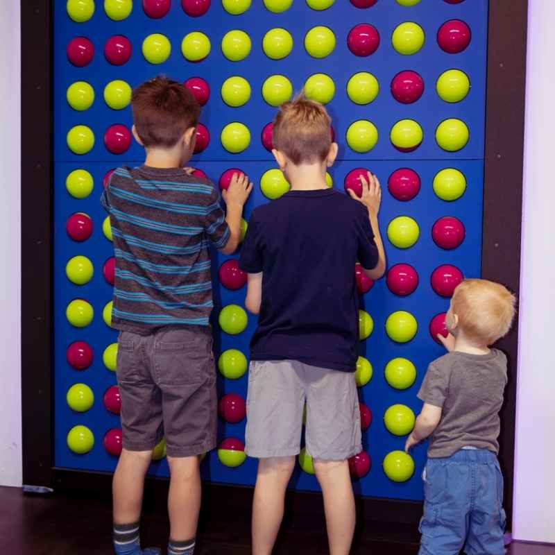 Children interacting with the LiteZilla Spinfinity Wall interactive spinning wall panel, pressing pink and green sphere shapes