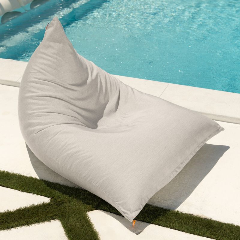 Jaxx Twist Outdoor Bean Bag Chair in Sunbrella Flax at the edge of a pool, a warm neutral Sunbrella bean bag ready for outdoor or indoor lounging