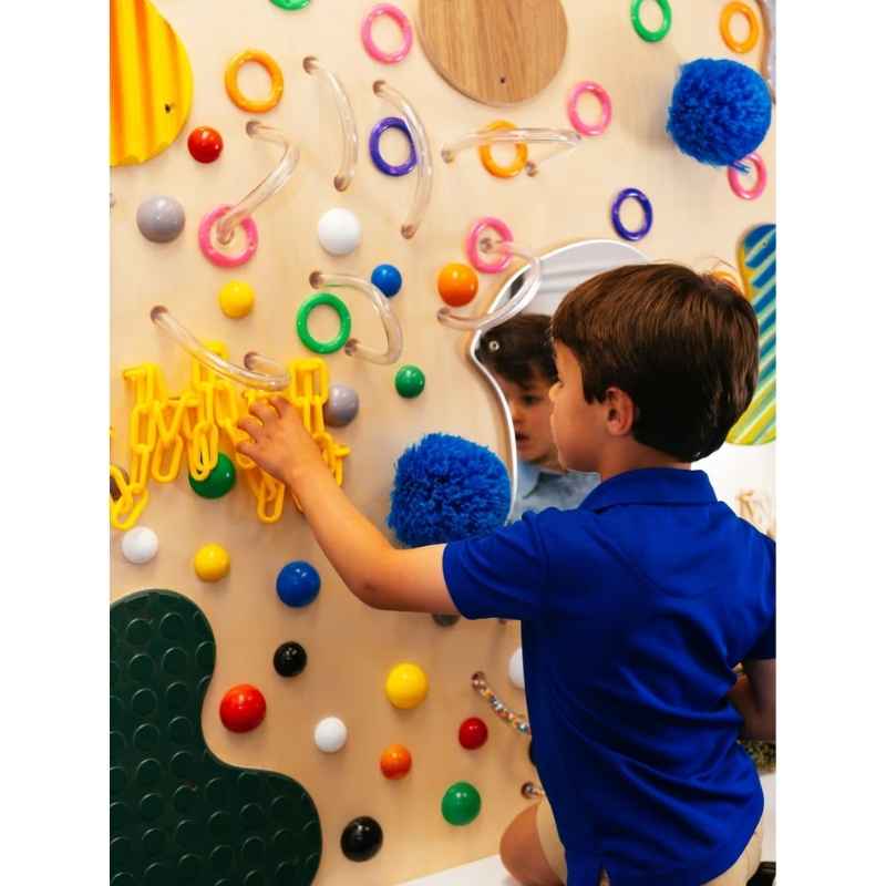 A child reaching for the yellow loop texture on the TFH Textured Wall Panel, a sensory wall panel designed for hands-on tactile play