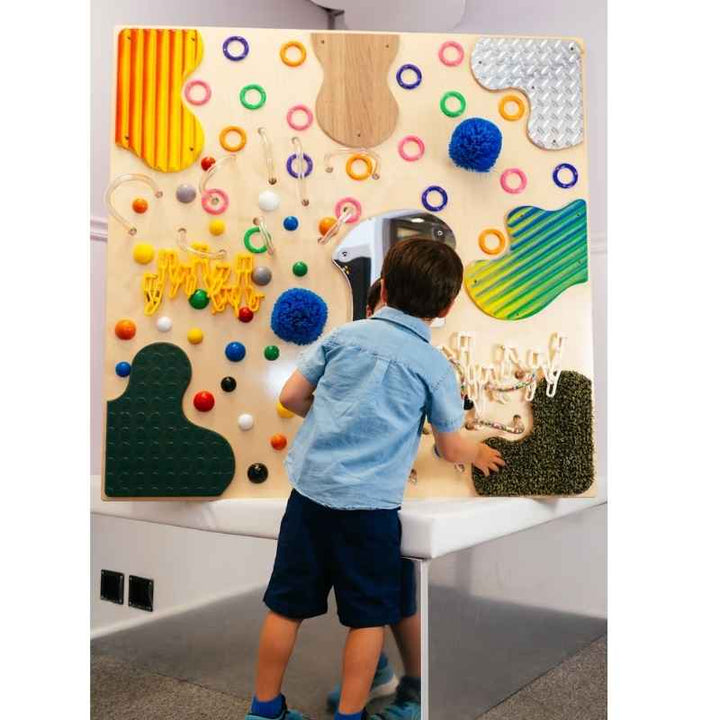A child standing at the TFH Textured Wall Panel exploring corrugated and looped textures on this sensory wall panel for therapy and home use