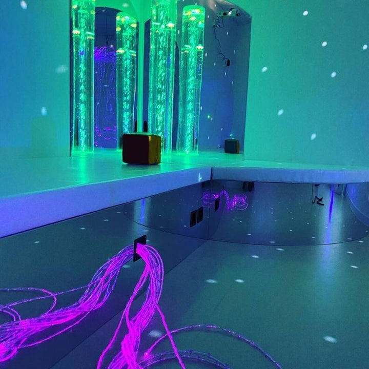 TFH Bubble Tube Corner Seat Base with bubble tube in aruba blue LED light showing the mirrored podium reflecting sensory room colours