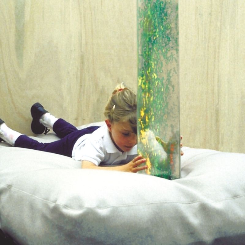 Child in active sensory play alongside TFH Bubble Tube Cuddle Cushion demonstrating the body-contouring beanbag surround for close-proximity bubble tube sensory engagement