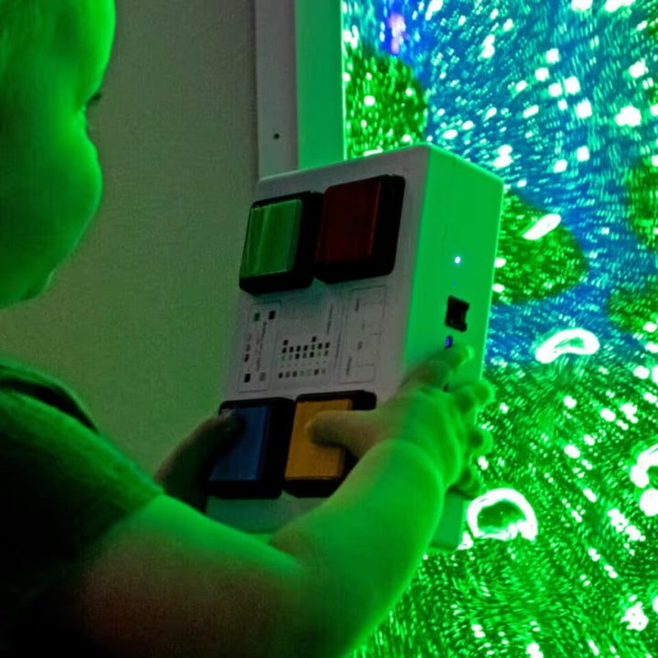 A child holds a four button colour controller in front of a TFH Bubble Wall lit in green, showing switch compatible colour control