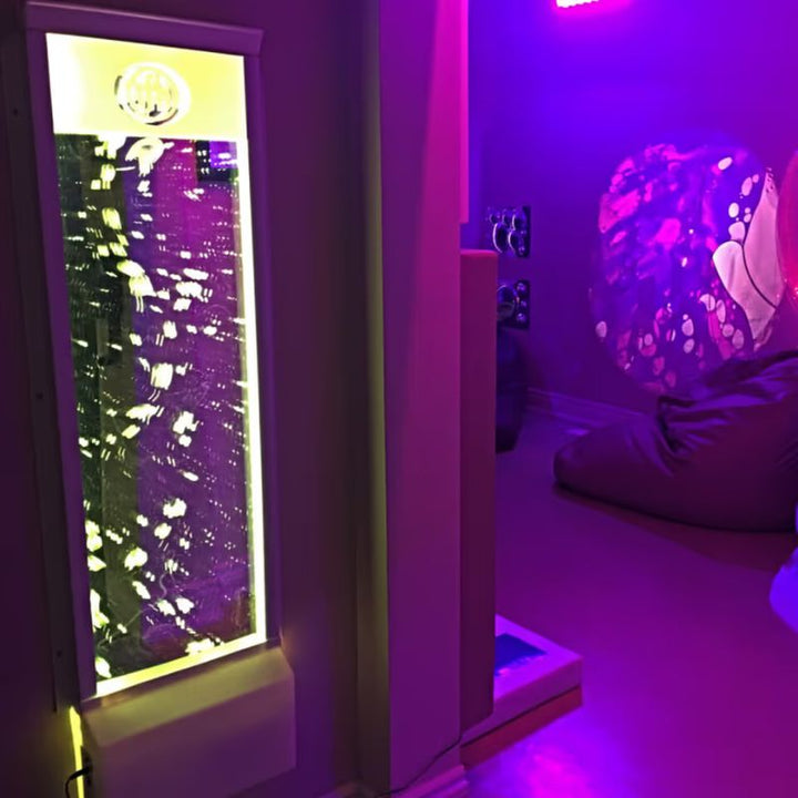 A TFH Bubble Wall lit in yellow and purple in a relaxed sensory lounge area with bean bag seating nearby