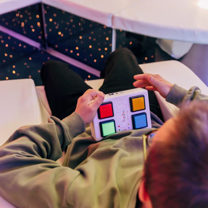 Person using the TFH Wired Colour Controller in a sensory room with fibre optic lighting, showing hands-on colour control in action