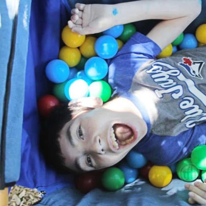 A child relaxing inside the TFH Deep Boat Swing surrounded by sensory balls, enjoying the calming vestibular motion of this enclosed swing