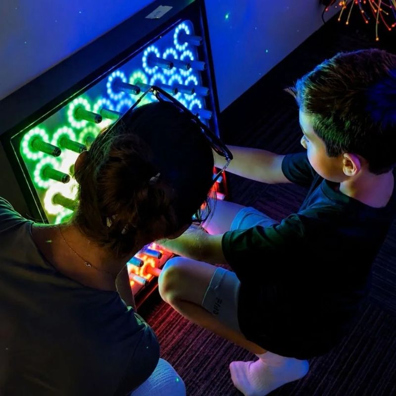 Adult and child exploring the TFH Electro Wobble Garden Activity Panel together, green, blue and orange rings of light responding to each spring they touch
