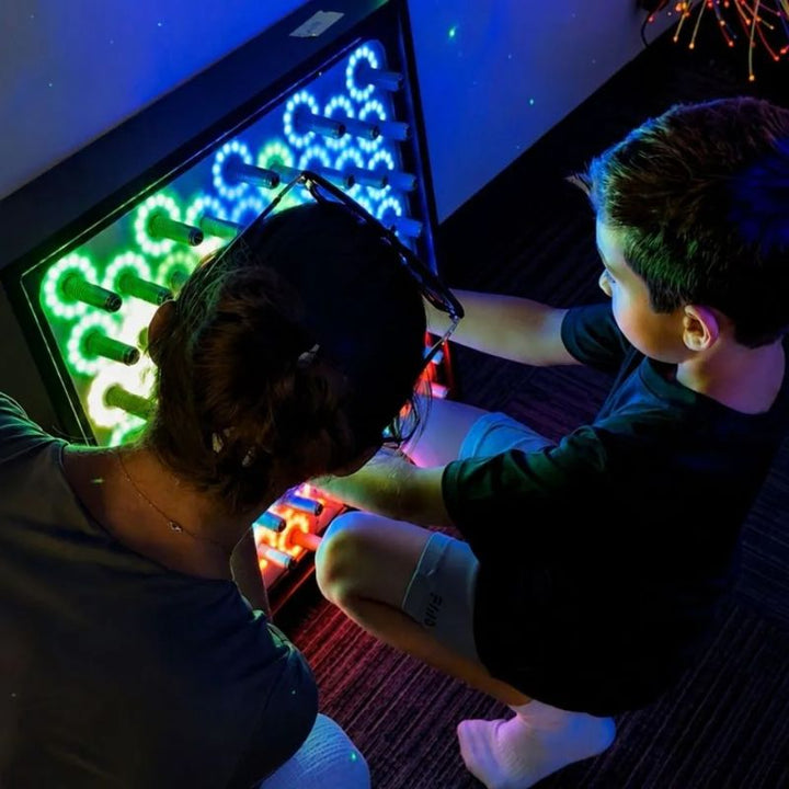 Adult and child exploring the TFH Electro Wobble Garden Activity Panel together, green, blue and orange rings of light responding to each spring they touch