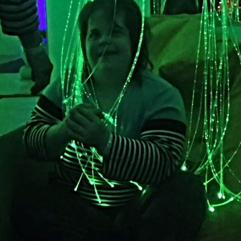 Adult actively engaging with TFH Fibre Optic Tails in a sensory room, showing visual and tactile sensory stimulation