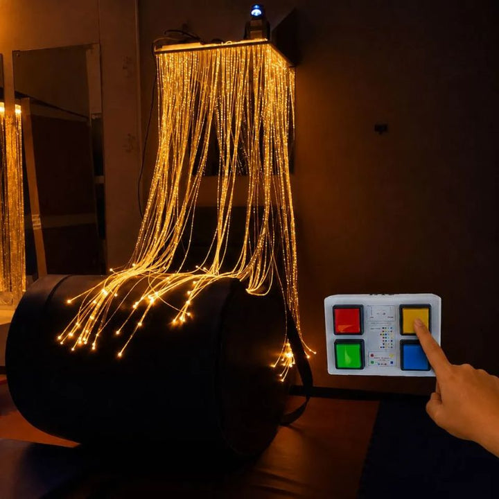 Hand pressing the 4-button wireless controller of the TFH Fibre Optic Waterfall Wireless Button Box System, the tails glowing amber in a sensory room