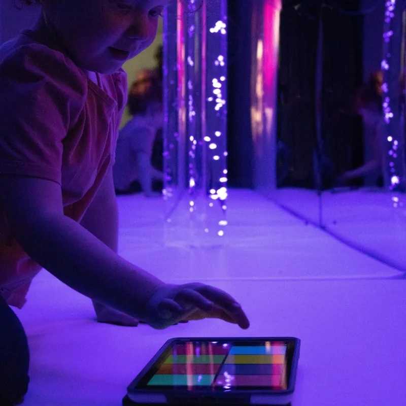 Child using an iPad with the TFH Genie Receiver app to control bubble tubes in a darkened multi-sensory room