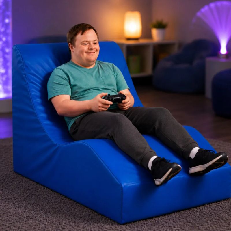 Smiling adult playing a video game while reclining in the blue TFH Giant Foam Relax & Recline Regular/Senior size, an ergonomic foam sensory lounger for calm, supported rest