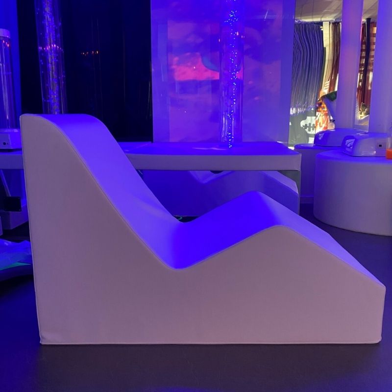 TFH Giant Foam Relax & Recline shown from the side in a dim sensory room setting, demonstrating the ergonomic reclined foam positioning shape for therapy and relaxation