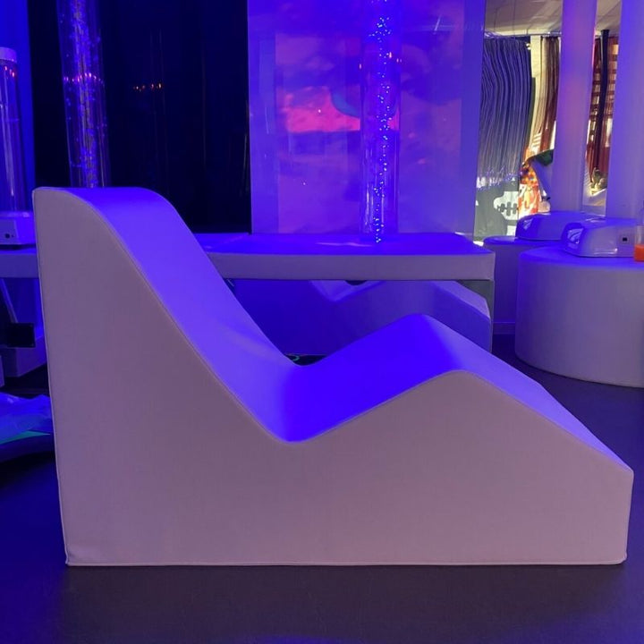 TFH Giant Foam Relax & Recline shown from the side in a dim sensory room setting, demonstrating the ergonomic reclined foam positioning shape for therapy and relaxation