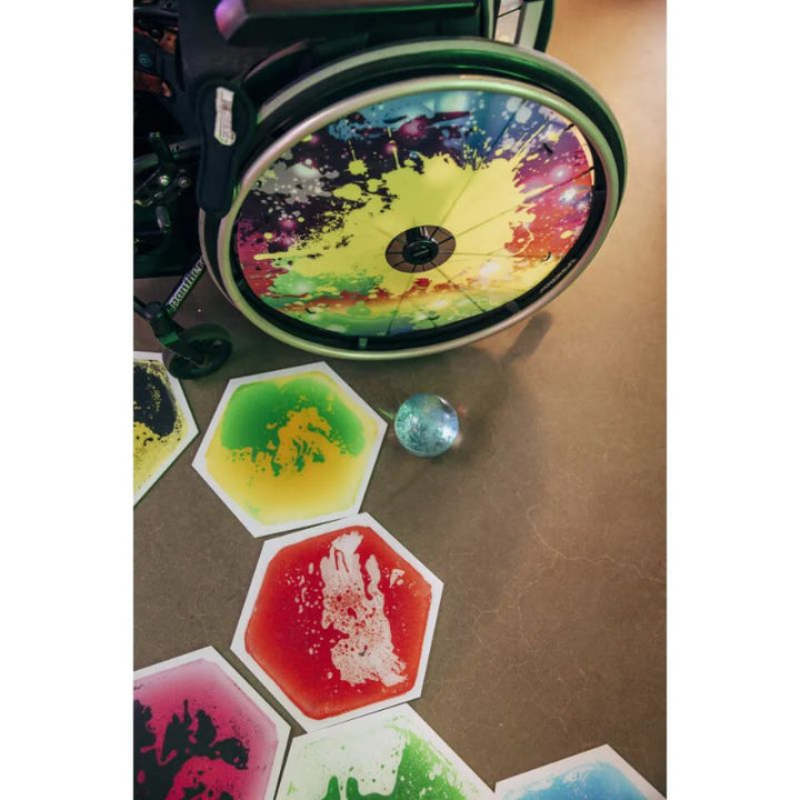TFH Hexagon Liquid Floor Tiles 9 Set in green, yellow, red and blue swirls on the floor beside a wheelchair, colourful sensory floor tiles for visual and tactile exploration