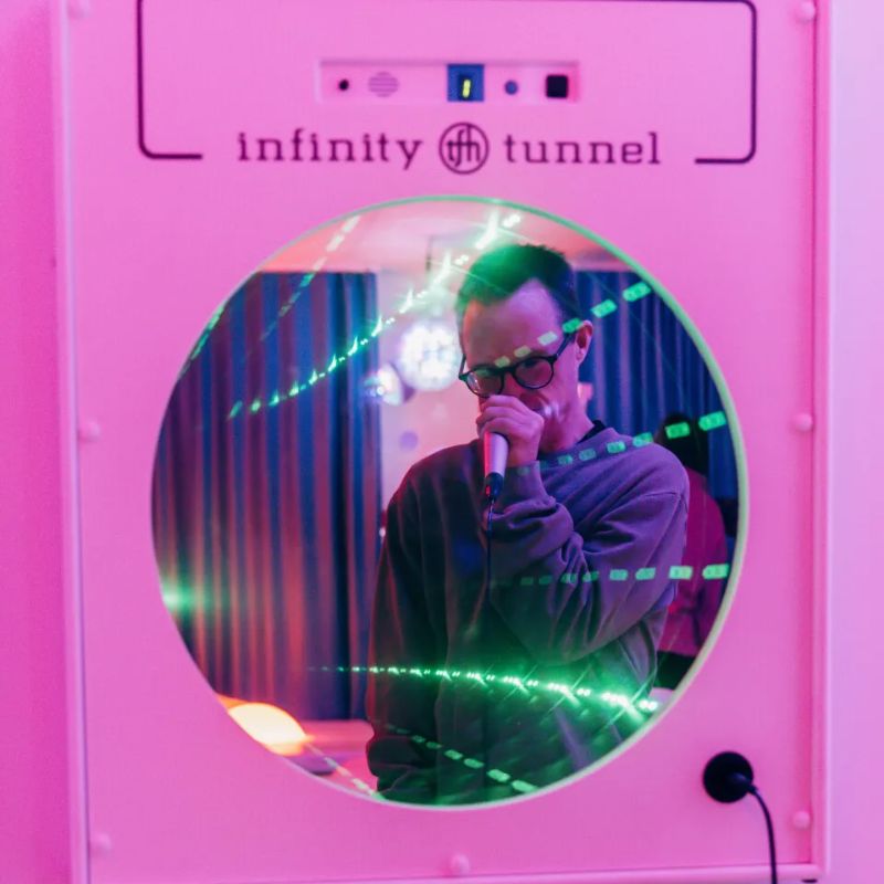 Man singing into the microphone, reflected in the pink-lit TFH Interactive Infinity Tunnel as green light trails react to his voice for vocalization play