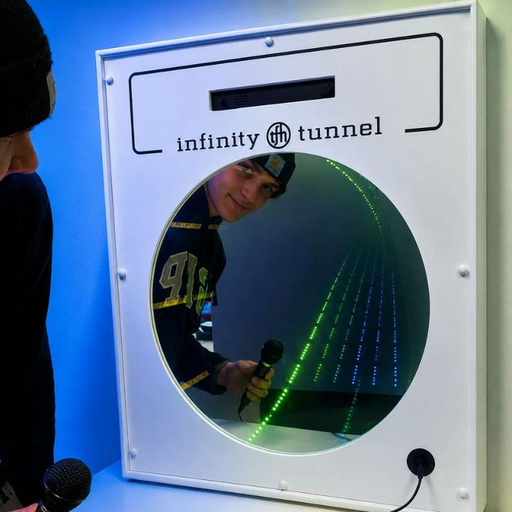 Teen holding the included microphone and smiling at his reflection in the TFH Interactive Infinity Tunnel, green and blue LED rows stretching into the optical illusion