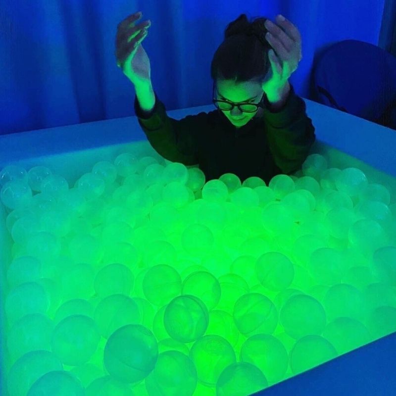 Girl playing inside the TFH Large Light-Up Ball Pit surrounded by glowing translucent sensory balls in green and blue LED light