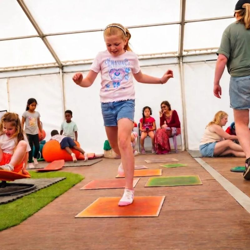 Girl hopping across the TFH Large Square Liquid Floor Tiles 4 Set in orange and green, sensory floor tiles that turn movement into active, colourful group play
