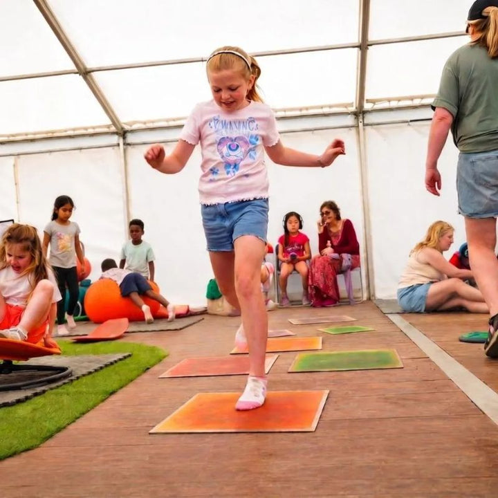 Girl hopping across the TFH Large Square Liquid Floor Tiles 4 Set in orange and green, sensory floor tiles that turn movement into active, colourful group play