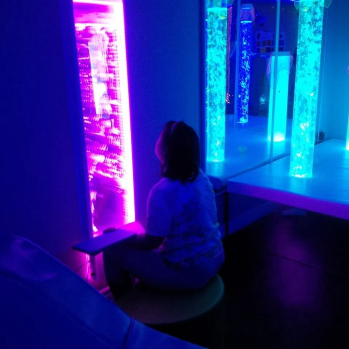 Child sitting close to watch the TFH Lights & Bubbles Water Panel glowing purple in a multi-sensory room, a space-saving bubble wall for visual tracking and calm