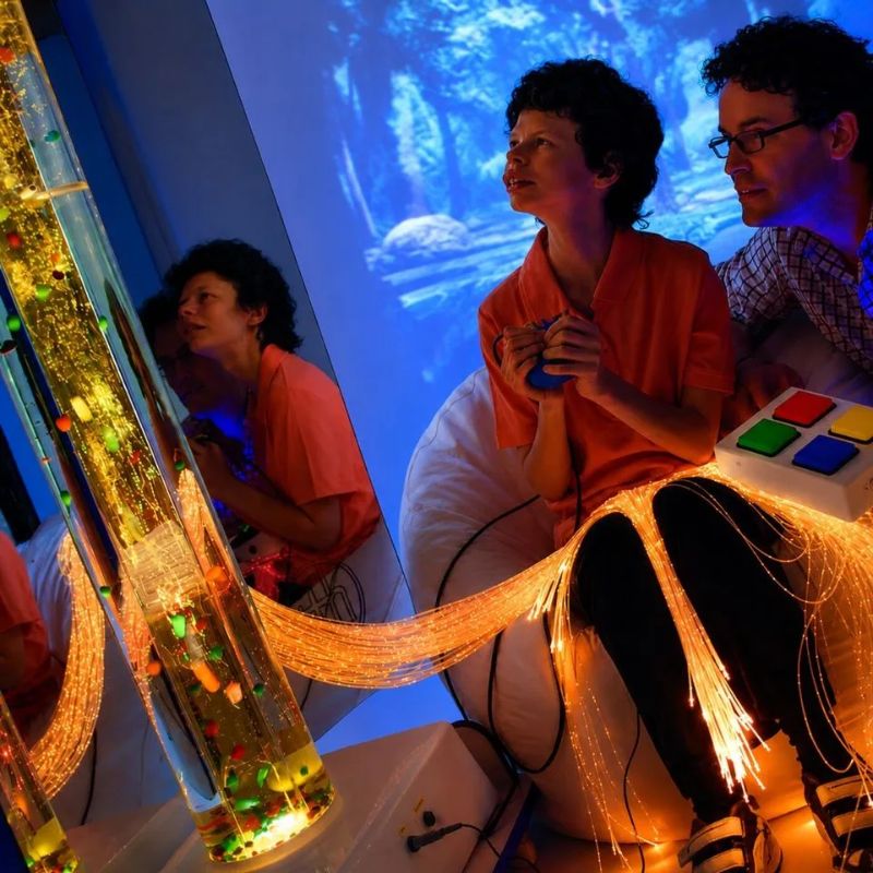 Man and woman interacting with the TFH Mobile Sensory Cart Deluxe fibre optic tails glowing red during a sensory therapy session