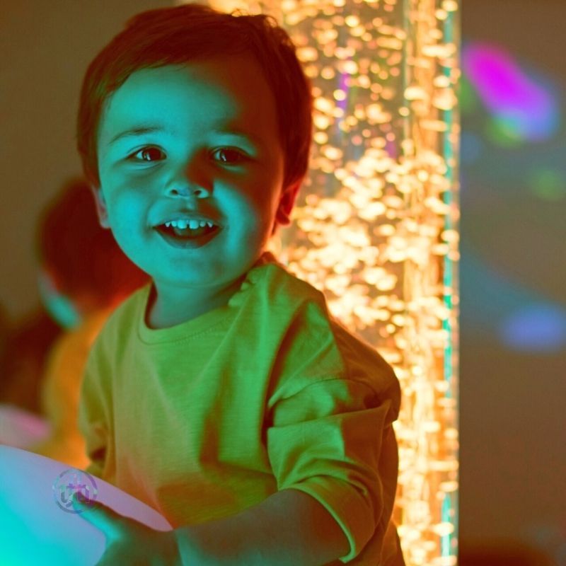 Smiling child playing with the TFH Interactive LED Bubble Tube, showing the calming and engaging sensory room experience