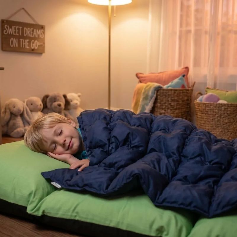 Child sleeping peacefully under the navy TFH Sensory Pressure Vinyl Ball Pad, a deep pressure sensory pad that offers calming comfort for rest and relaxation
