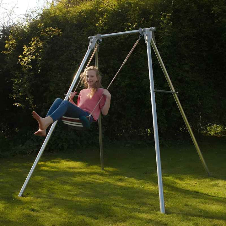Child swinging on a fabric seat attached to the TFH Sensory Swing Frame set up outdoors in a backyard sensory space