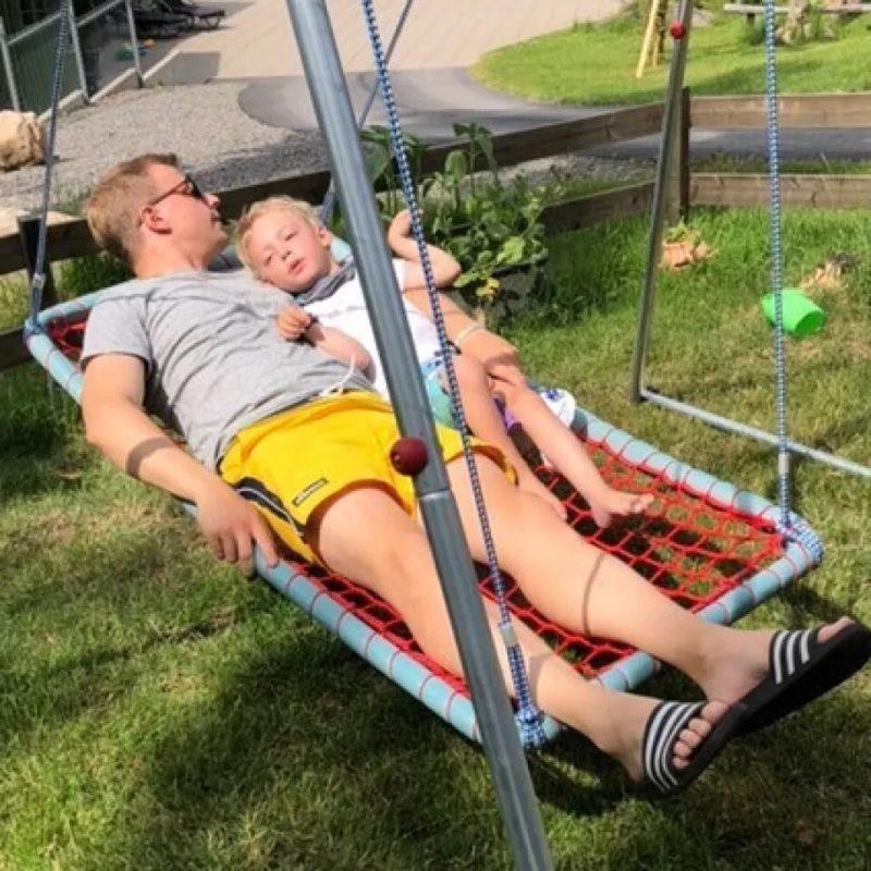 Father and child relaxing together in the TFH Sky Cruiser Net Swing outdoors, showing the 55" framed hammock sensory swing's room for shared vestibular rest