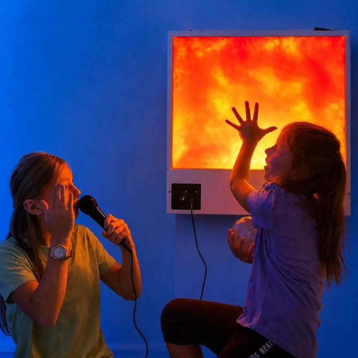 Two girls sharing the TFH Sound to Light Interactive Panel, one singing into the microphone while the other reaches toward the orange glow, a sound-responsive sensory panel for turn-taking