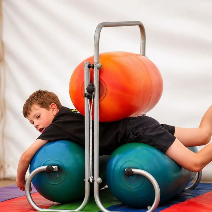 Boy squeezing through the TFH Sensory Squeeze Machine between an orange top bumper and two teal bumpers, enjoying full-body deep pressure input on a padded mat